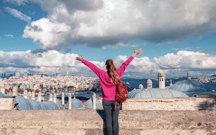 Person overlooking Istanbul skyline near Galata Tower, arms raised in excitement.