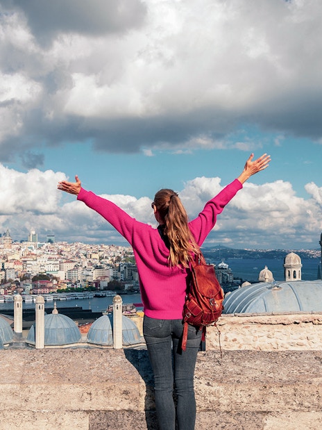 Person overlooking Istanbul skyline near Galata Tower, arms raised in excitement.