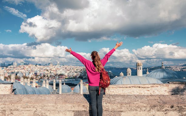 Person overlooking Istanbul skyline near Galata Tower, arms raised in excitement.
