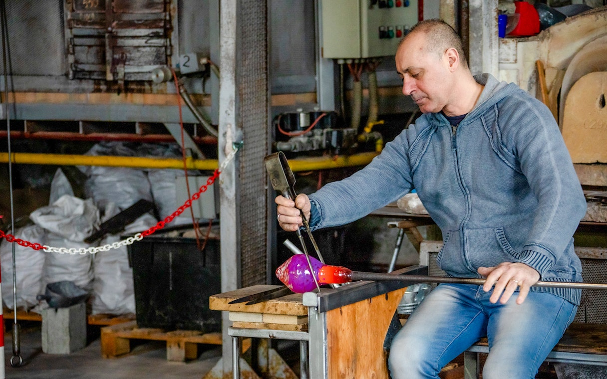 Glassblower crafting colorful glass in Murano workshop, Venice.