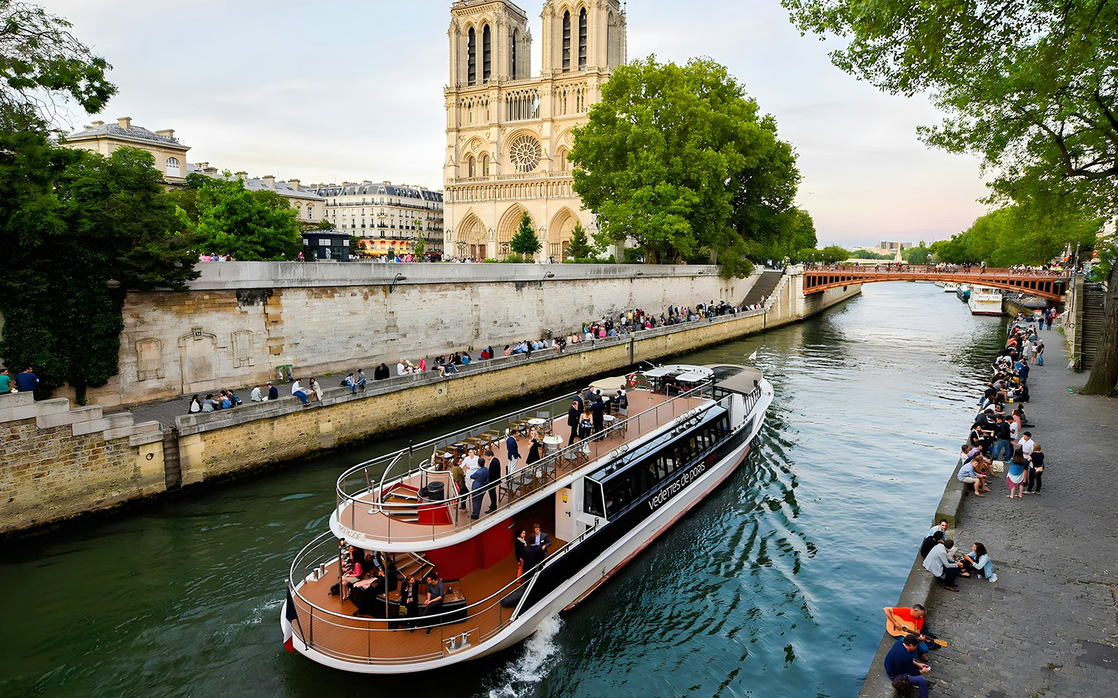 Vedettes de Paris cruise passing Notre Dame with people enjoying the Seine River, Paris.