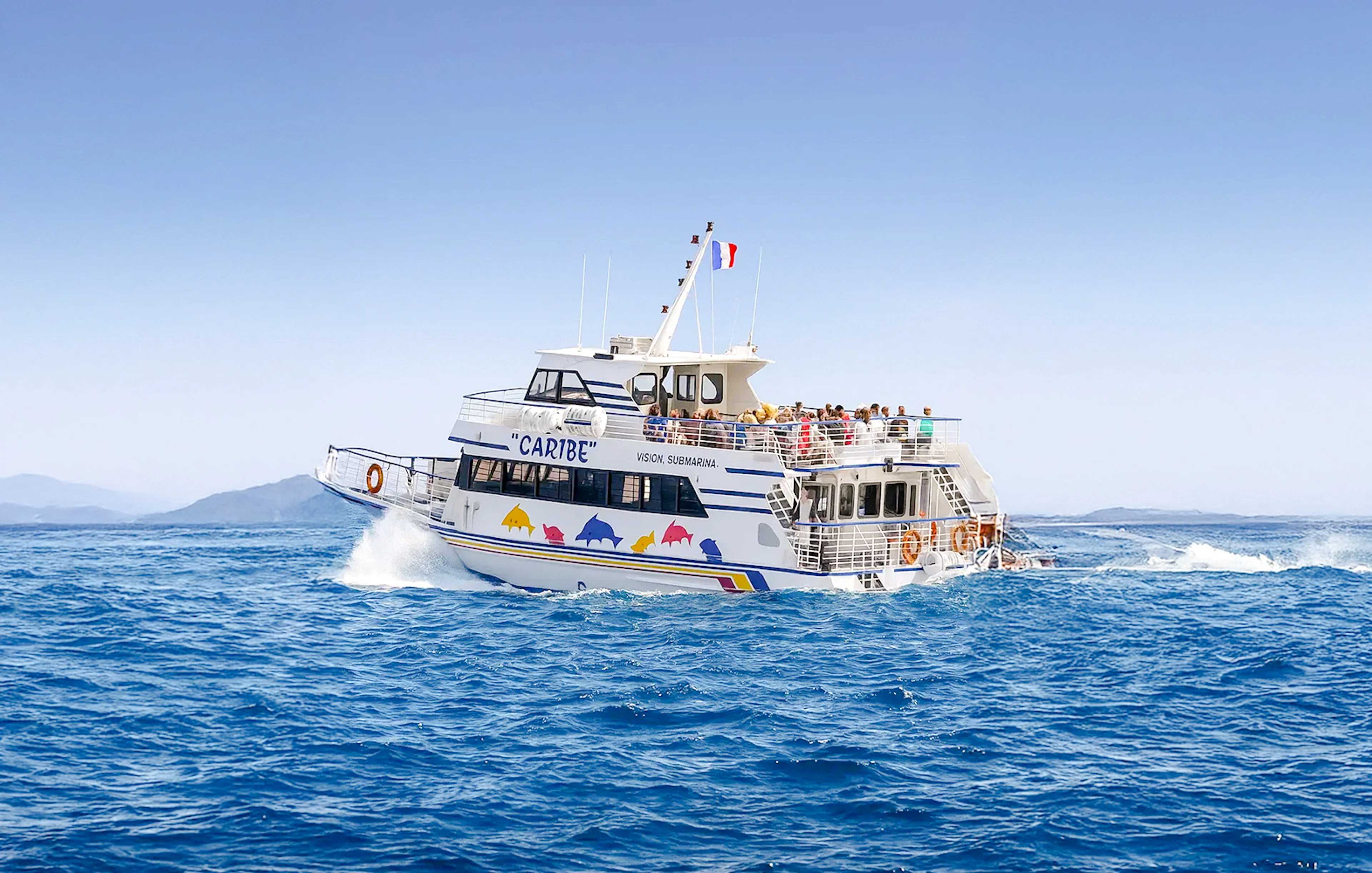 Tourists on a sightseeing cruise boat in Nice, France, with distant mountains.