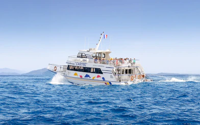 Tourists on a sightseeing cruise boat in Nice, France, with distant mountains.