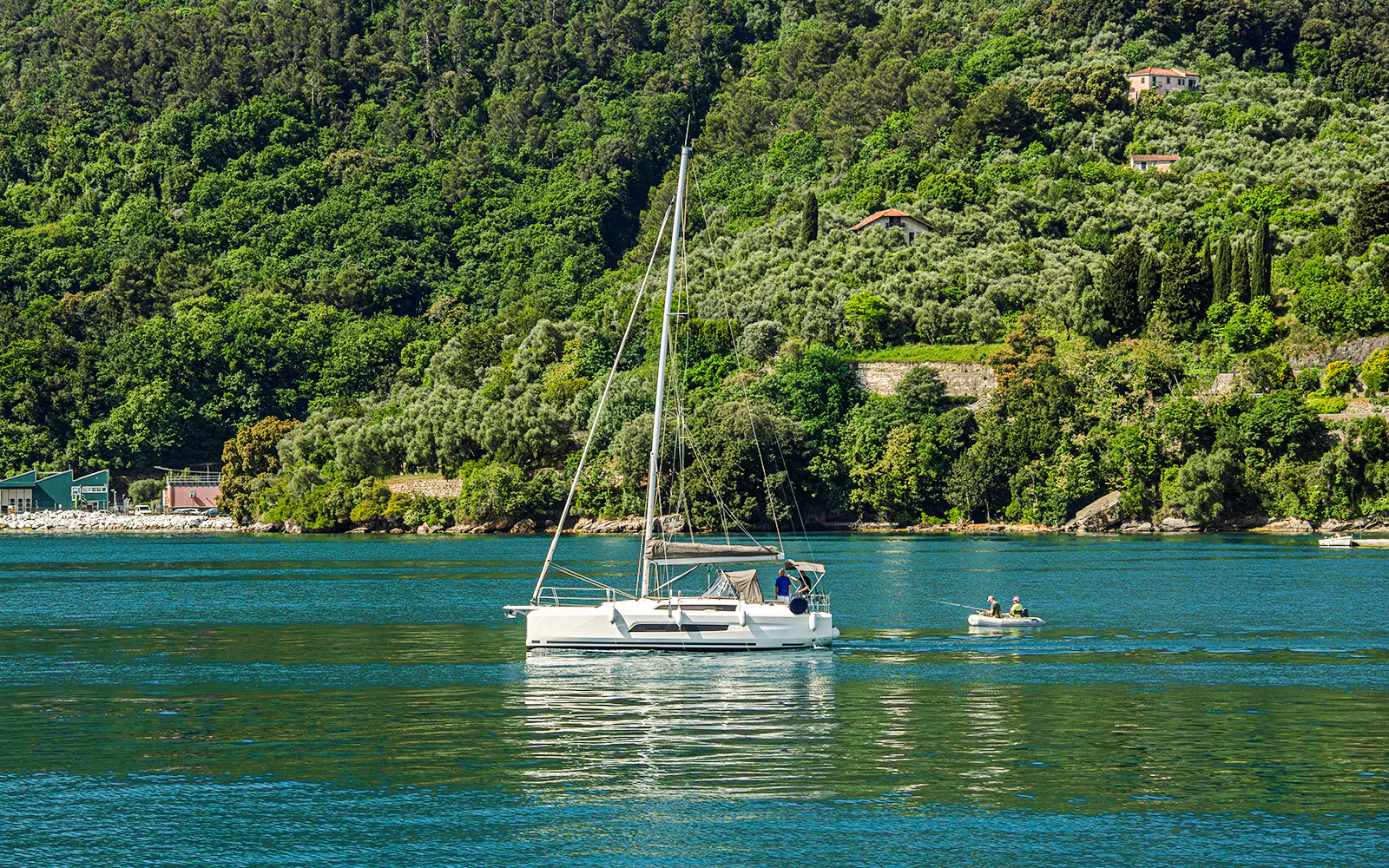 Yacht cruising past a fishing boat on a scenic lake with lush green hills.