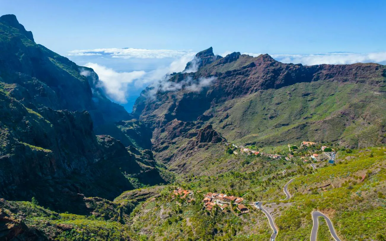 Masca Village nestled in lush green mountains, Tenerife, with winding roads and distant peaks.
