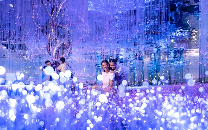 Visitors exploring Celestia inside AYA Universe with glowing lights and reflective surfaces.