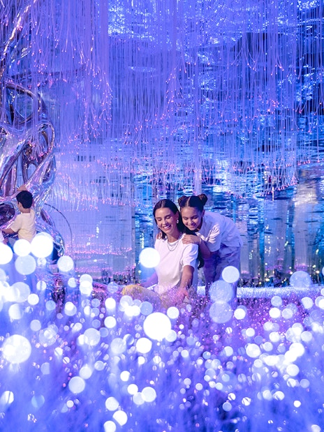 Visitors exploring Celestia inside AYA Universe with glowing lights and reflective surfaces.