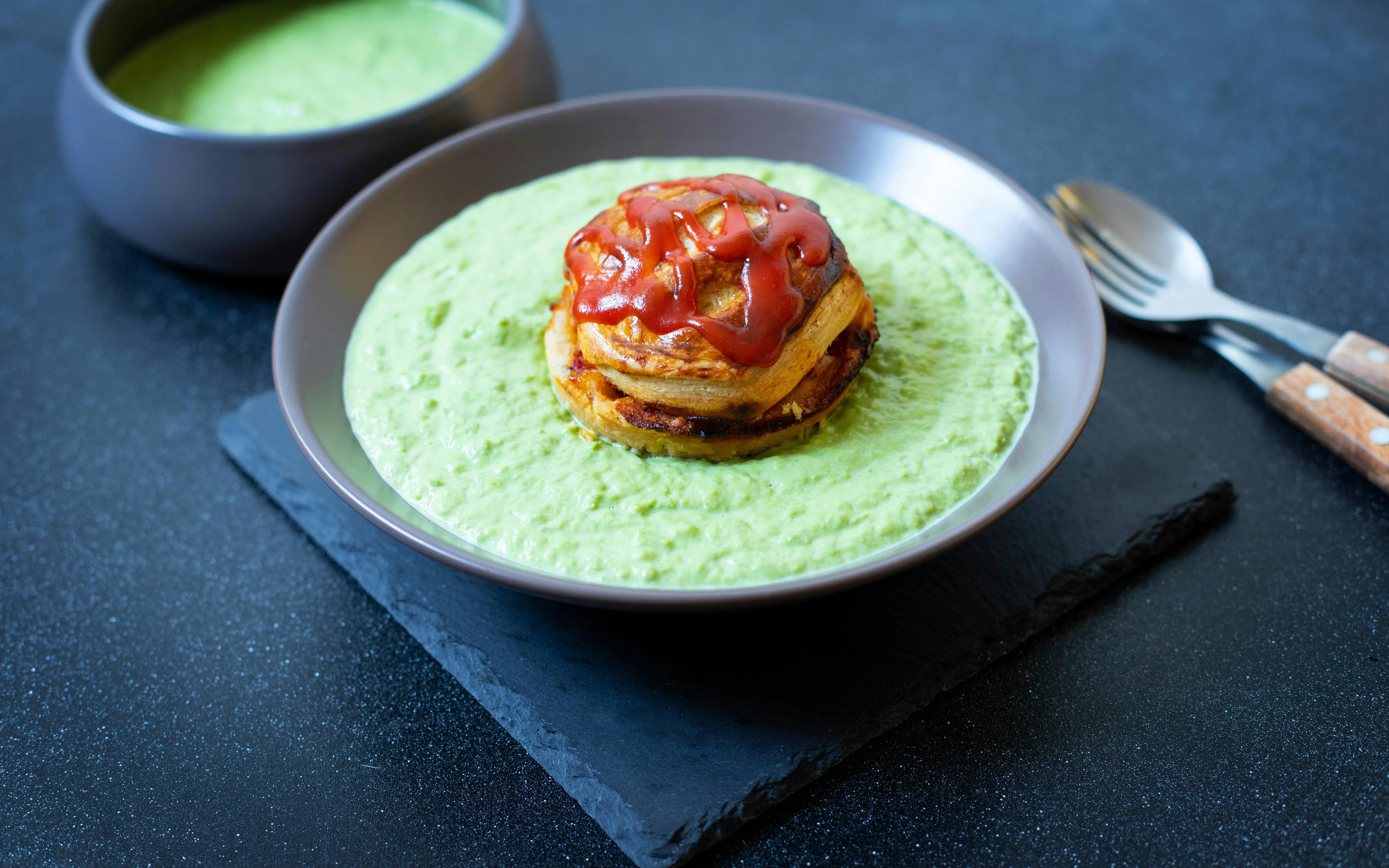 Traditional Australian pie floater with meat pie in green pea soup on black background.