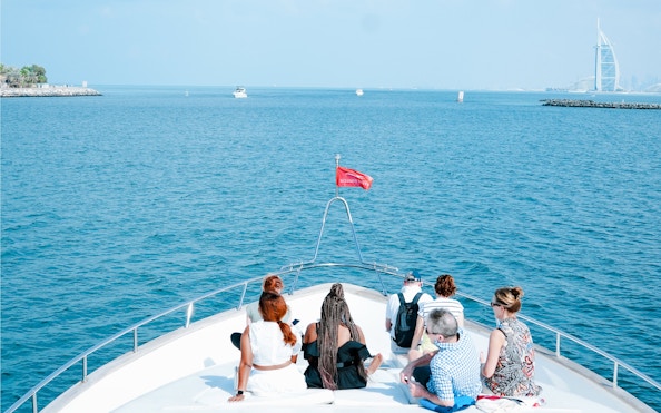 Tourists on a yacht in Dubai Harbour with Burj Al Arab in the background.