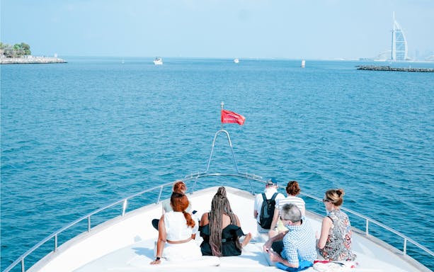 Tourists on a yacht in Dubai Harbour with Burj Al Arab in the background.