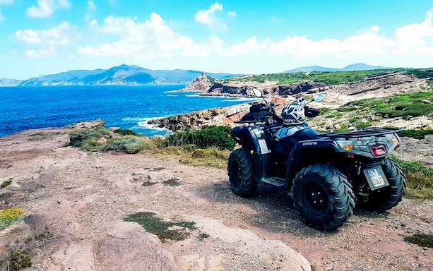 Quad bike on coastal trail in Alghero, Sardinia with sea and cliffs in background.