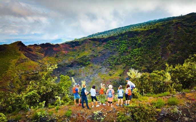 Guests observing Hualalai volcano crater with guide in Hawaii.