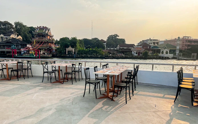 Tables set for dining on The Luxury White Dinner Cruise at ICONSIAM, overlooking the river and cityscape.