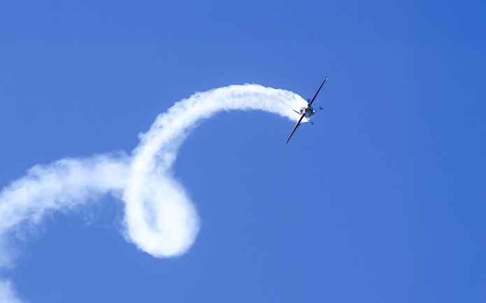 Aerobatic plane performing a loop with smoke trail in clear blue sky.