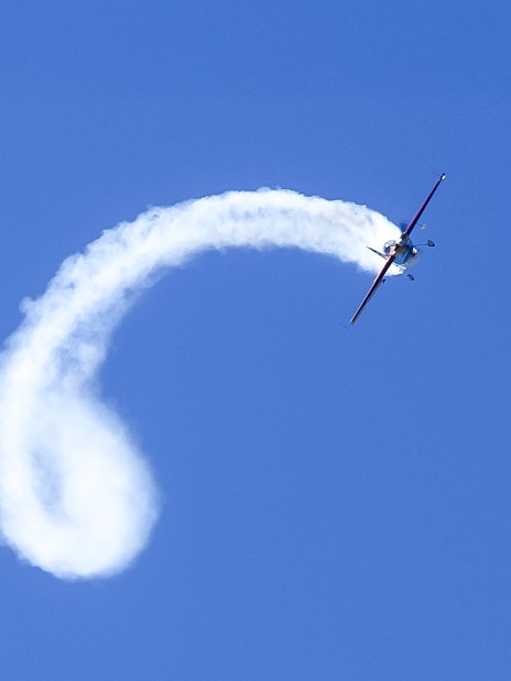 Aerobatic plane performing a loop with smoke trail in clear blue sky.