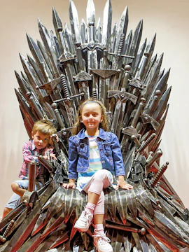 Children sitting on a steel throne at the Gallery Of Steel Figures.