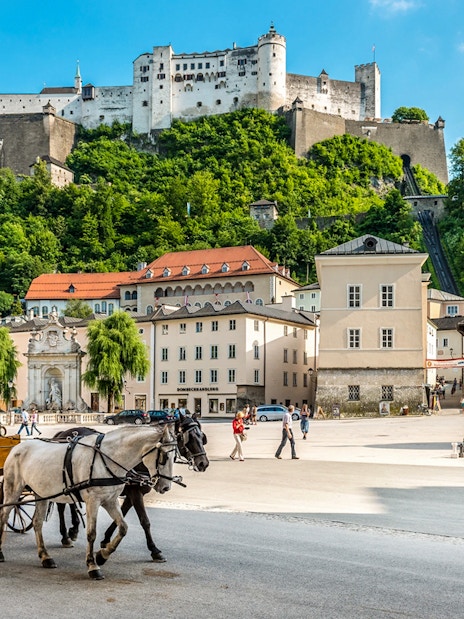 Horse-drawn carriage in Salzburg's Kapitelplatz with Hohensalzburg Fortress in the background.