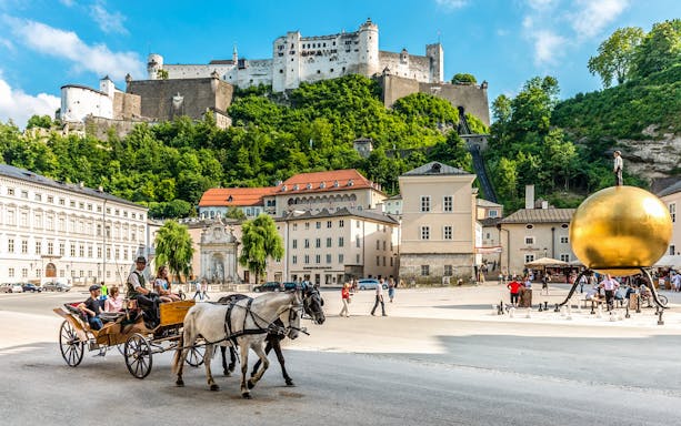 Horse-drawn carriage in Salzburg's Kapitelplatz with Hohensalzburg Fortress in the background.