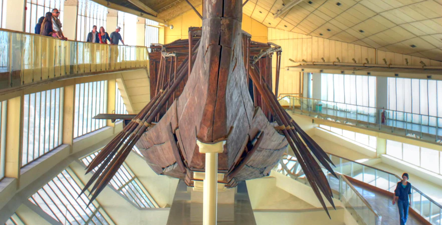 Khufu's Solar Ship displayed in the Grand Egyptian Museum with visitors observing.