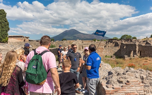 Tour group exploring Pompeii ruins with Mount Vesuvius in the background.