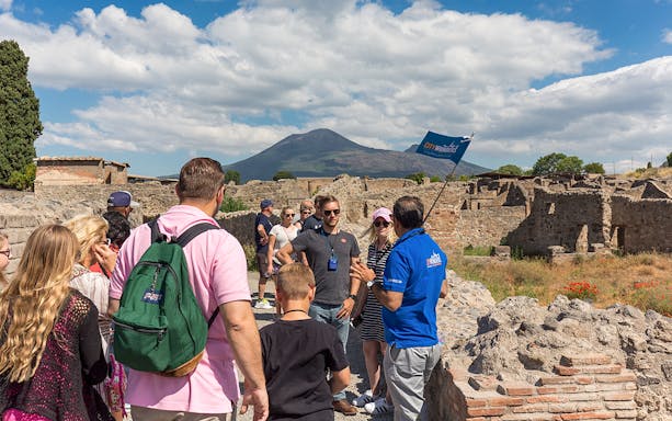 Tour group exploring Pompeii ruins with Mount Vesuvius in the background.