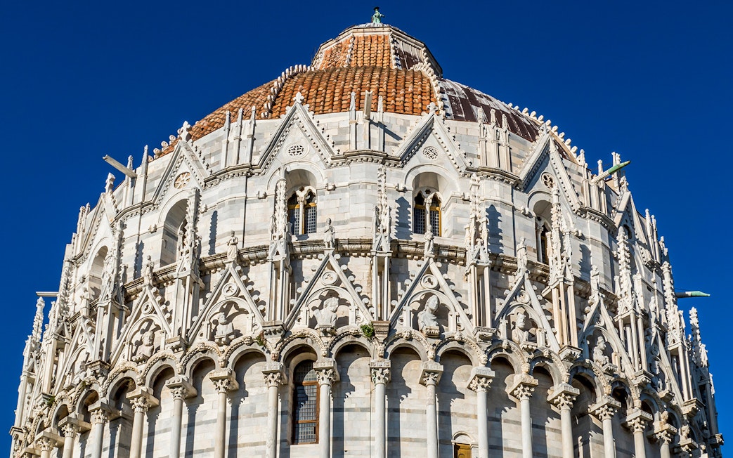 Baptistery of Pisa with detailed Gothic architecture under a clear blue sky.