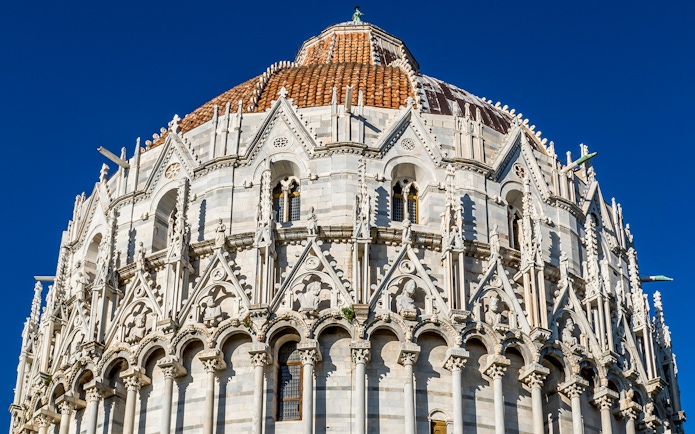 Baptistery of Pisa with detailed Gothic architecture under a clear blue sky.
