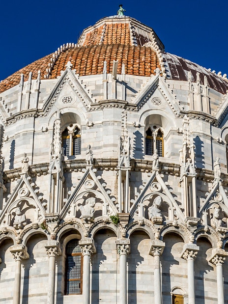 Baptistery of Pisa with detailed Gothic architecture under a clear blue sky.