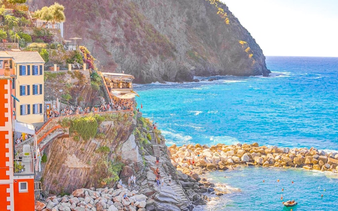 Cliffside view of colorful buildings and tourists in Cinque Terre, Italy, overlooking the sea.