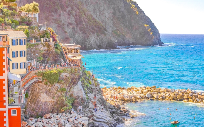 Cliffside view of colorful buildings and tourists in Cinque Terre, Italy, overlooking the sea.
