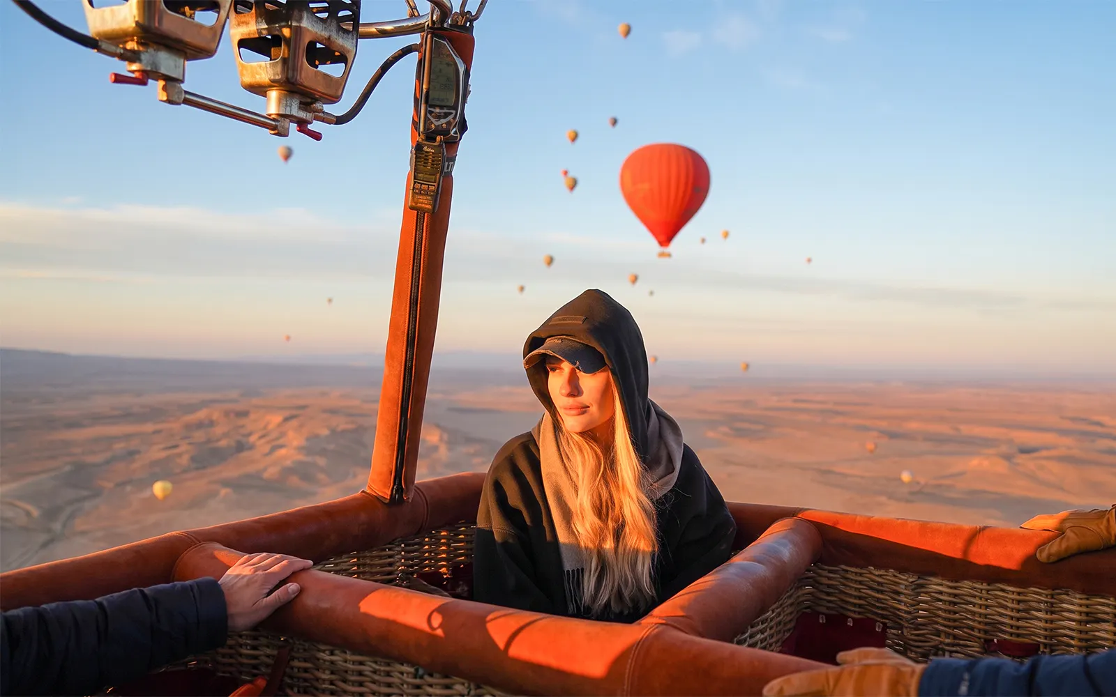 Hot air balloon over Marrakesh desert at sunrise with passenger and distant balloons.