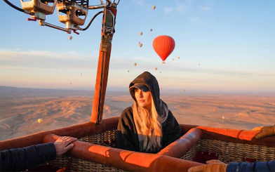 Hot air balloon over Marrakesh desert at sunrise with passenger and distant balloons.