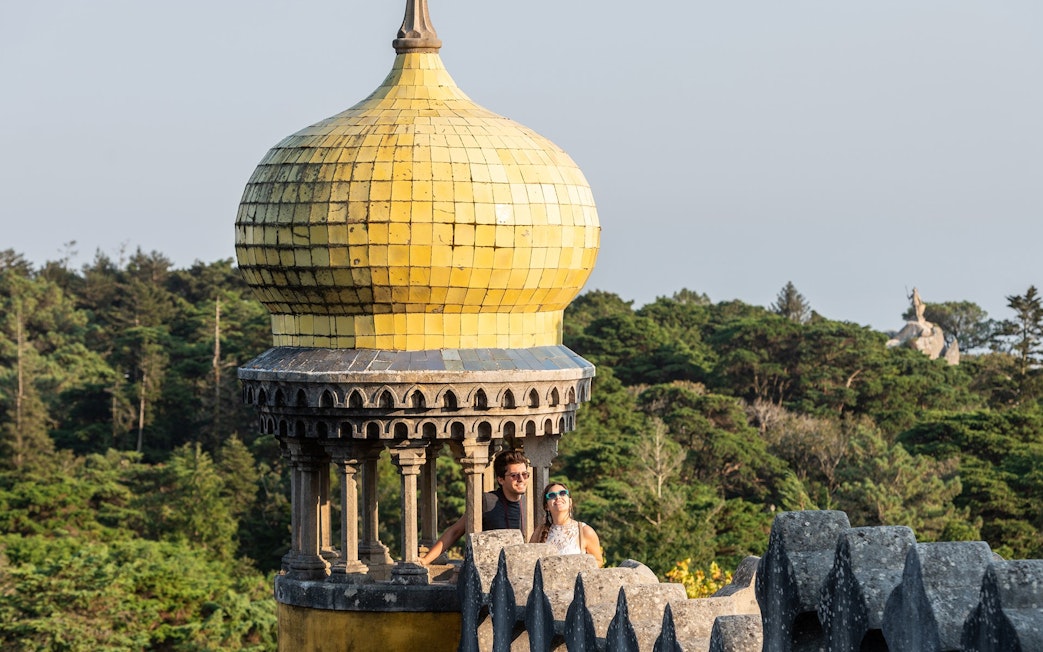 Couple on terrace of Pena Palace, Sintra, with yellow dome and forest backdrop.
