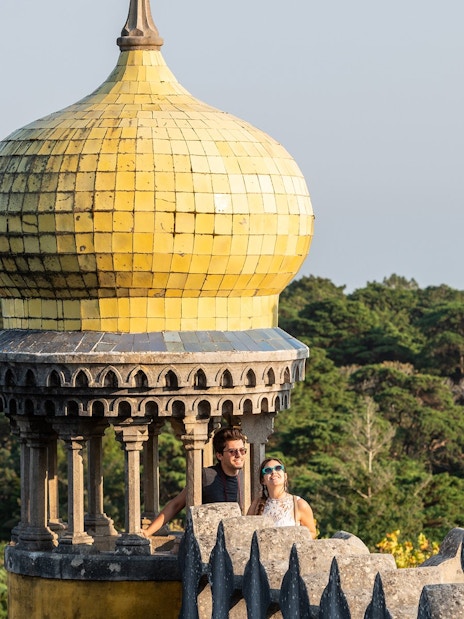 Couple on terrace of Pena Palace, Sintra, with yellow dome and forest backdrop.