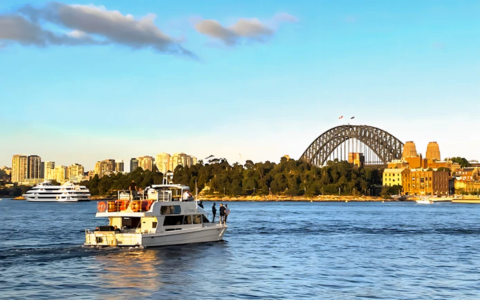 Cruise boat on Sydney Harbour with Sydney Harbour Bridge at sunset.