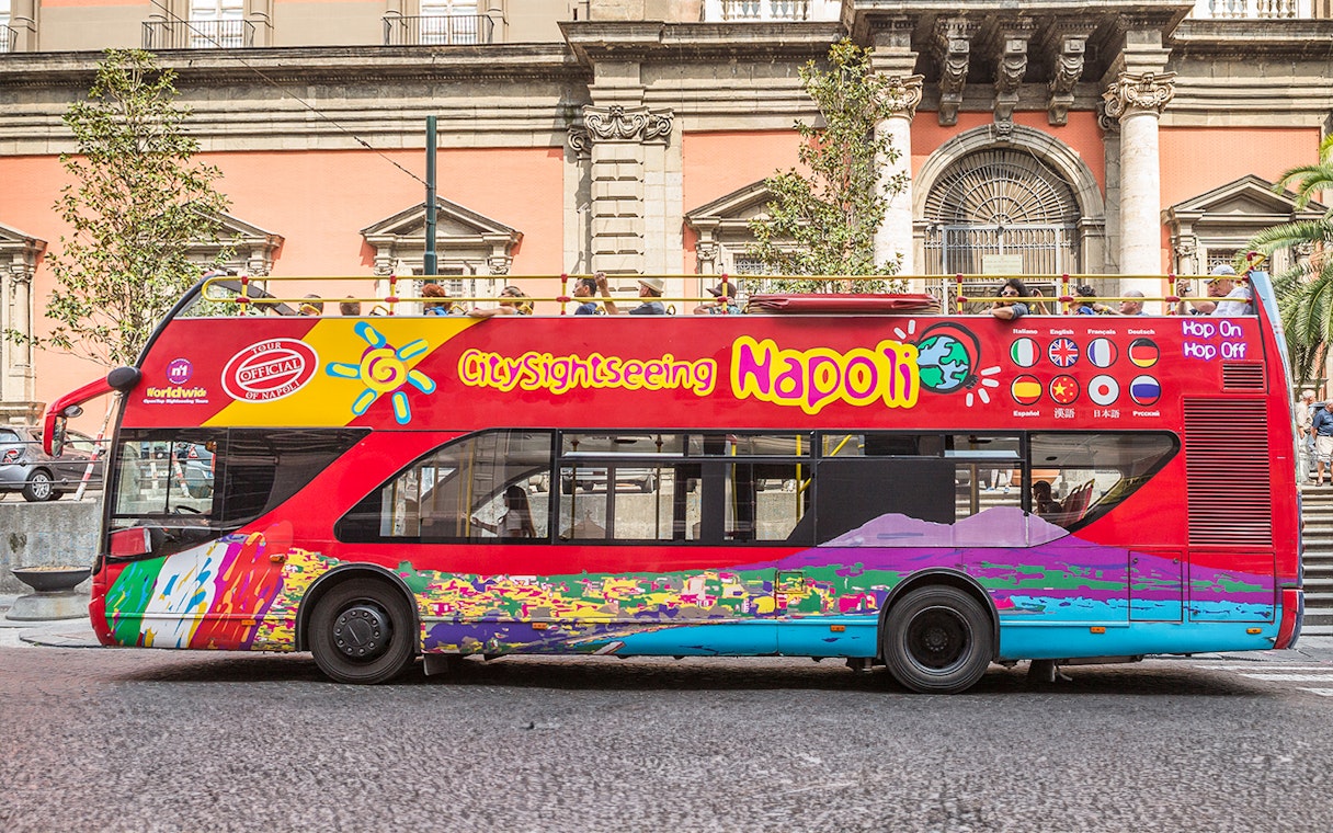 Hop-on hop-off tour bus in Naples, Italy, near historical architecture.
