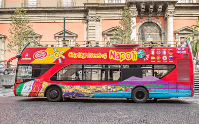 Hop-on hop-off tour bus in Naples, Italy, near historical architecture.