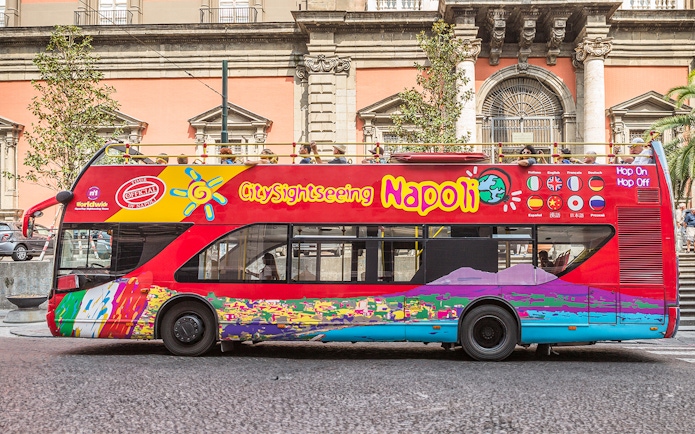 Hop-on hop-off tour bus in Naples, Italy, near historical architecture.