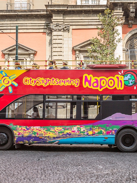 Hop-on hop-off tour bus in Naples, Italy, near historical architecture.