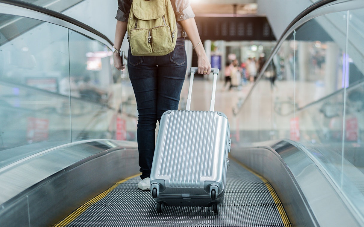 Traveler with suitcase on airport escalator.