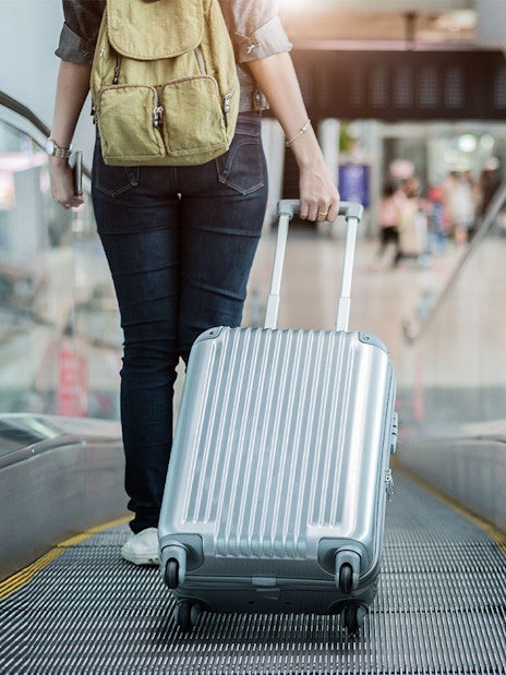 Traveler with suitcase on airport escalator.