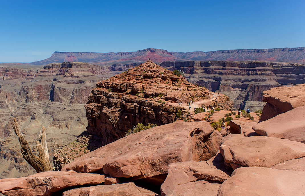 Grand Canyon West view with tourists on rocky path, clear sky in background.