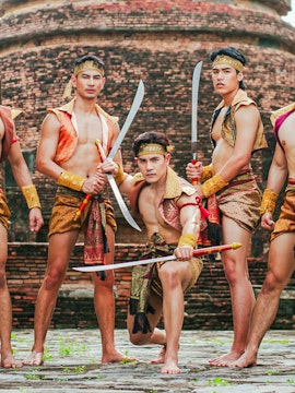 Traditional Thai warriors in historical attire with swords at an ancient temple in Ayutthaya, Thailand.