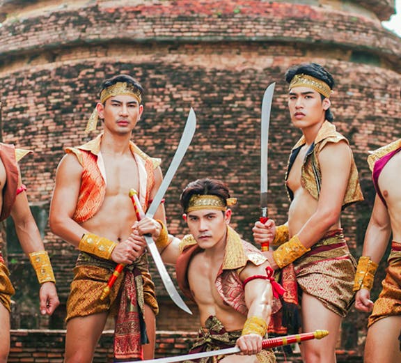 Traditional Thai warriors in historical attire with swords at an ancient temple in Ayutthaya, Thailand.