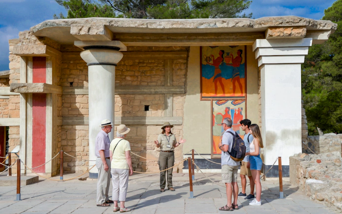 Tour group with guide at Knossos Palace, Crete, viewing ancient frescoes.