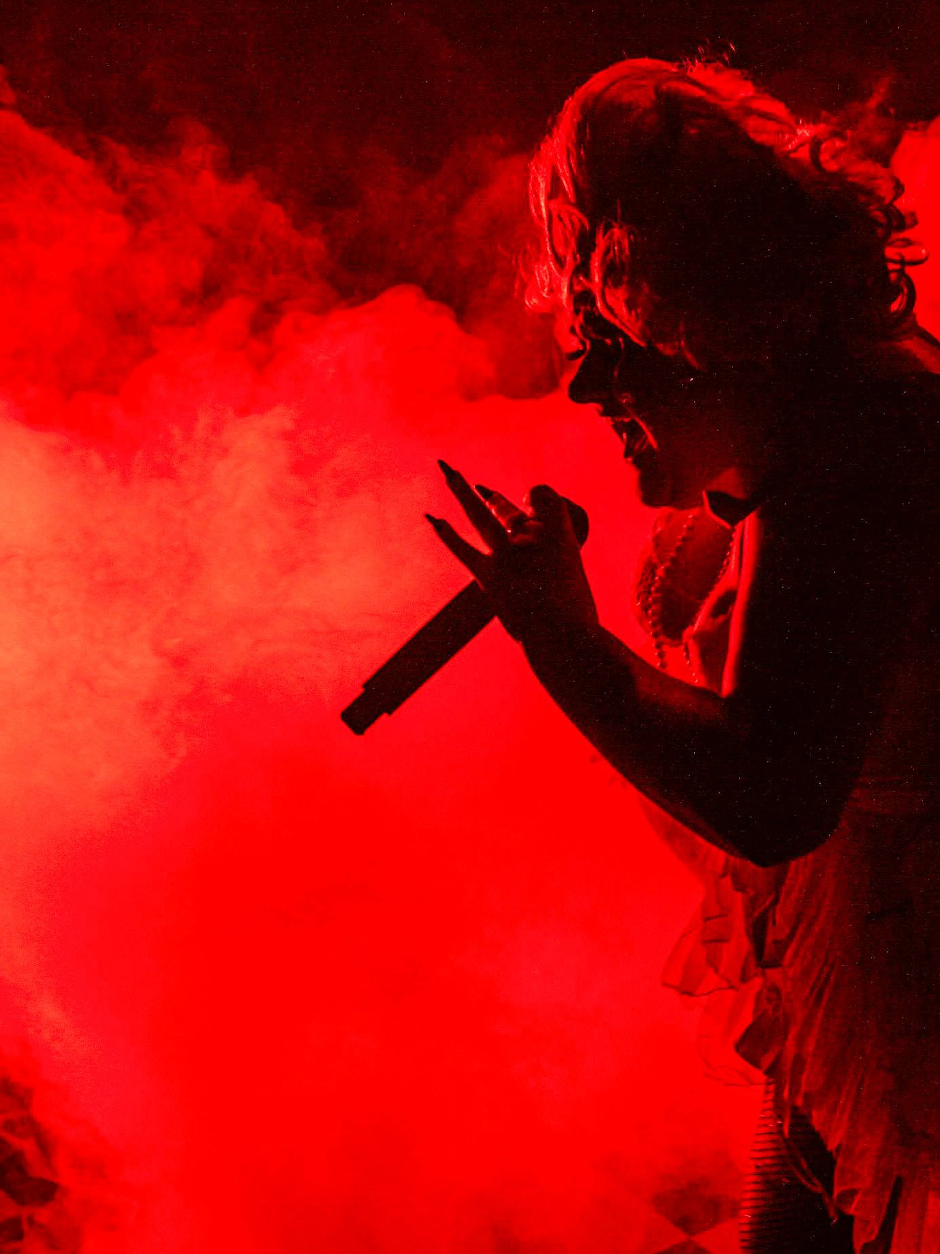 Performer singing at Madame Arthur cabaret show in red stage lighting.