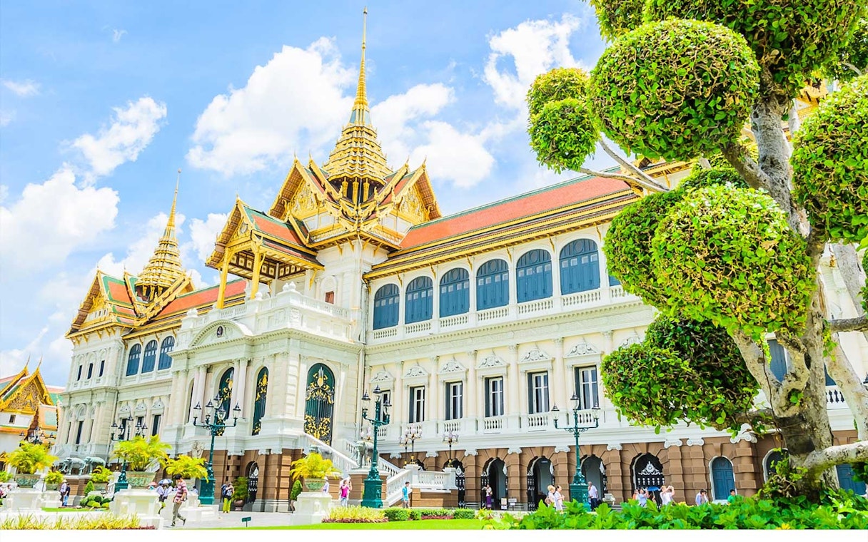 Grand Palace in Bangkok with ornate architecture and manicured trees.