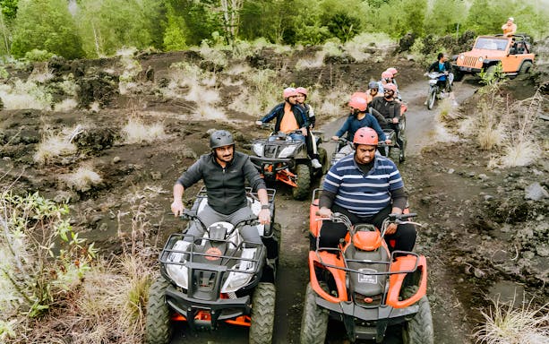 Group riding ATVs on rocky terrain in Kintamani, Bali, with lush greenery in the background.