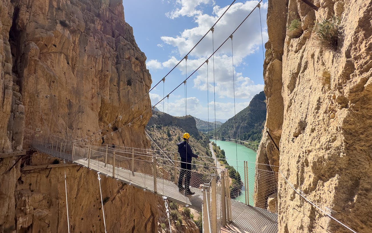 Hiker on suspension bridge at Caminito del Rey with cliffs and river view, Malaga day trip.
