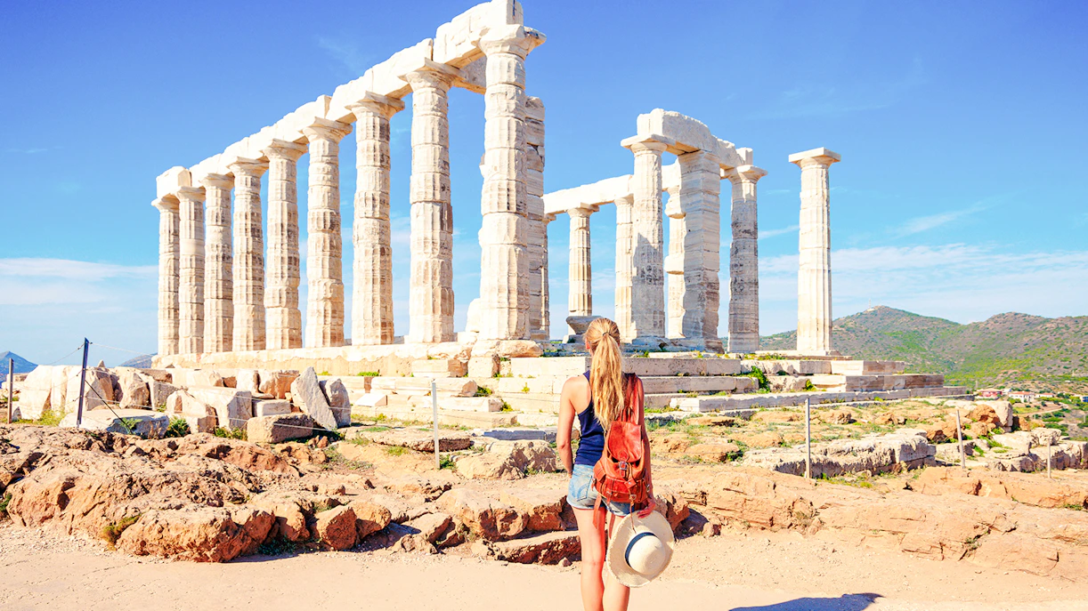 Visitor at Temple of Poseidon, Sounion, Greece, with ancient columns and scenic landscape.